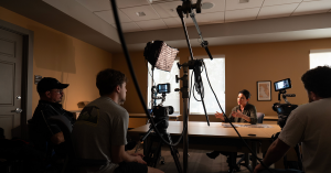 The director and crew sit amongst gear and lights, interviewing a subject for The Ringling Ghost