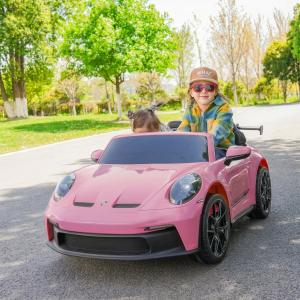 Two children ride in a pink 24V Porsche 911 GT3 2-seater electric ride-on car from LA Toyz on a sunny outdoor path.