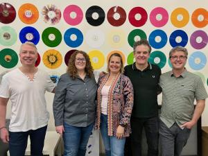 Citizen Vinyl’s leadership team is pictured standing in front of a wall of colorful vinyl records.