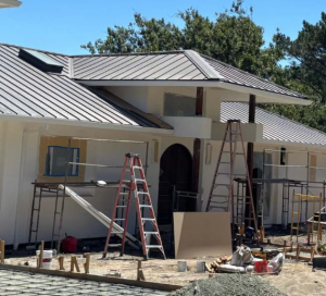 A house with scaffolding and ladders set up for exterior renovation, featuring a partially completed metal roof and construction materials in the yard.