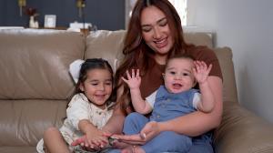 Danika Gonzales sits on a sofa next to her three-year-old daughter while holding her six-month-old son.