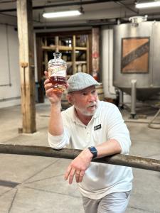 Peerless Distilling Co. tour guide, Kentucky Ken, sharing the history of the distillery. He stands in the historic brick and wood barrel room, showcasing the craftsmanship of the spirits.