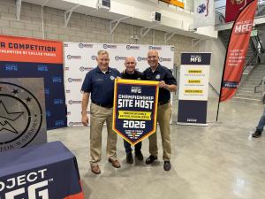 Lyle Palm and Hernán Luis y Prado stand with Dan Gazzano while receiving a Project MFG Championship Site Host banner recognizing Workshops for Warriors as host of the 2026 Maritime Welding and National Welding League Championships in San Diego.