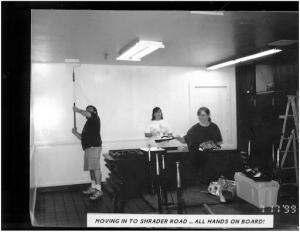A black and white image of parent volunteers using paintrollers on the ceiling of a small classroom. The image has a caption "MOVING IN TO SHRADER ROAD ... ALL HANDS ON BOARD!"
