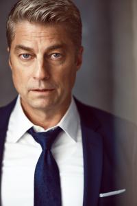 Photo of actor Jamison Jones wearing a suit and staring directly into the camera.