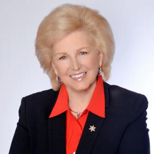 Pictured is a headshot of Opal Singleton, a smiling white woman with blonde hair, wearing a black blazer and bright red point collar with a gray background. She is author of the book "Digital Warfare: Our Kids on the Frontline" with https://MillionKids.org 
