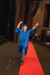 Photo of graduate walking across stage with his arms up in the air