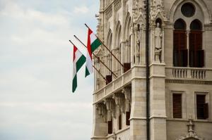 Hungarian national flags flying on the historic stone facade of a prominent government building in Budapest, representing the country's institutional stability.