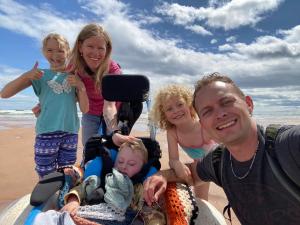 A family of five on the beach smile to the camera