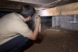 Pest control technician performing termite inspection in crawl space under Jacksonville Florida home with flashlight on wood joists