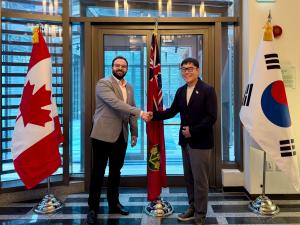 Essam Elsahwi and Felix Lee shake hands posing with Canadian, Korean, and Ontarian flags