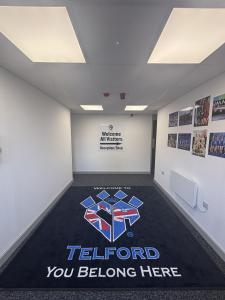 Entrance hallway inside the new Cheer Athletics Telford facility, featuring branded flooring, athlete achievement displays, and a welcoming reception area for athletes and families.