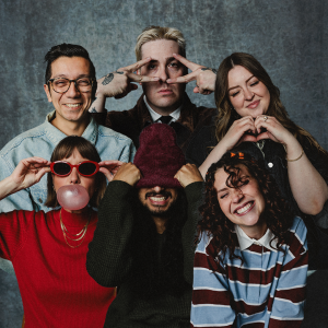 Six Life.Church Switch team members pose playfully for a group photo against a gray backdrop, each striking a different fun pose.