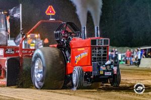 Red International Harvester tractor named Super Rooster pulling a sled during a nighttime tractor pulling competition.