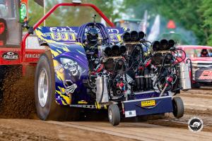 Multi-engine modified tractor pulling down a dirt track with four supercharged engines visible.