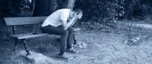 Photo of man sitting alone on a park bench with his head down appears very depressed in mental crisis
