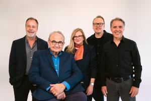 Group portrait of five BRC Imagination Arts team members. Left to right: Brad Shelton, Bob Rogers (seated), Carmel Lewis, Christian Lachel, and Matthew Solari, photographed against a white background.