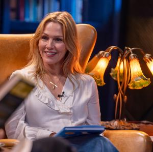 Jennie Garth sits in a high-backed library chair, holding a copy of Jonathan Livingston Seagull