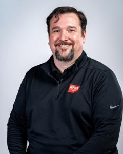 GPRS’ Market Segment Leader, Nate Baker, wearing a black quarter-zip pullover with a red GPRS logo on the chest, seated against a light gray background.