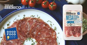 Texas Iberico Mesa Salami displayed alongside sliced salami on a white enamel plate, surrounded by Mexican oregano, tomatoes, and garlic. A Good Food Awards Winner 2026 badge highlights the product's national recognition in the Charcuterie category.