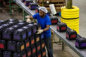 Worker handling wrapped beverage packaging on a production line inside a manufacturing facility.