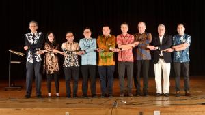 On the stage, dignitaries and organizers hold hands with arms crossed in a handshake style popularized by ASEAN meetings.