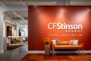 Entry area of CF Stinson Brands' new showroom at THE MART, featuring an oversized custom wallcovering, branded feature wall, orange lounge seating, and textile displays visible throughout the space.