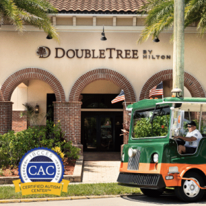 Entrance of DoubleTree by Hilton hotel with arched brick design, palm trees, American flags, and a green shuttle vehicle in the foreground.