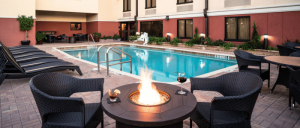 Outdoor pool area with black lounge chairs, wicker seats around a fire pit, and a building in the background.