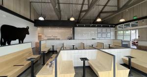Interior dining hall of a commercial restaurant with newly painted white shiplap walls, dark charcoal accent walls and trim, and an exposed painted wood-truss vaulted ceiling.