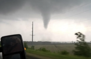 A tornado funnel touches down across a Kansas field, viewed from inside the Dominator intercept vehicle's side mirror.