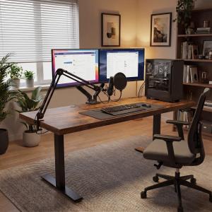 OffiGo 71-inch executive electric standing desk in a home office with dual monitors, microphone arm, keyboard, chair, and wide wood desktop.