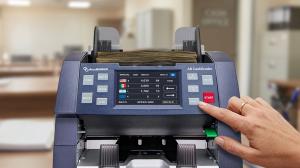 AccuBANKER AB8000 CashGrader bill counter being operated in a professional banking environment showing multi-currency touchscreen display and dual sorting pockets