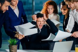 photo business man at his desk stressed out and screaming his subordinates all around him handing him papers