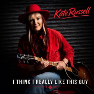 Cover art for Kate Russell's single "I Think I Really Like This Guy," featuring the singer wearing a red hat and red jacket while holding an acoustic guitar against a dark background.