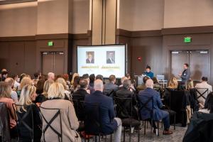 A Dickson Realty leadership presentation in a conference room with an audience of real estate professionals and a screen showing company leaders.