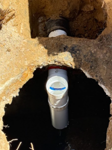 A view into a deep excavation showing newly installed PVC piping components for a professional sewer repair.