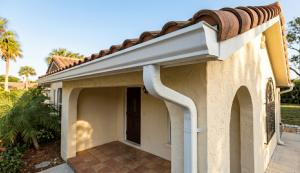 Close-up view of a home's entrance showcasing a tiled porch, decorative roof, and downspout against a clear blue sky.
