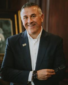 A professional image of Rick W. Wurth, CEO of OneQuest Health standing against a dark, wood paneled background.