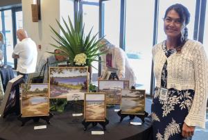 Artist Kris Garard stands at table displaying her plein air original art featuring coastal landscape