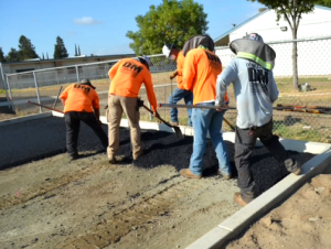 A construction crew wearing high-visibility shirts working together to spread asphalt during a site preparation and paving project.
