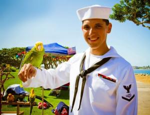 A White male in a sailor uniform and hat holding a parrot