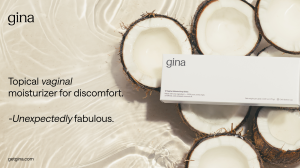 A sleek product photograph on a dark background displaying a white box of gina Vaginal Moisturizing Glides. Next to the box is a single, bullet-shaped solid coconut oil insert resting on a silver foil blister pack. The box text highlights features such as