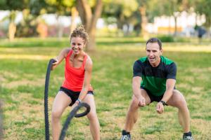 A smiling woman uses weighted exercise ropes as a man next to her instructs her.