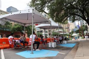 people sitting at tables and chairs under a shade structure on the Via Futbol pathway from Downtown to FIFA Fan Festival.