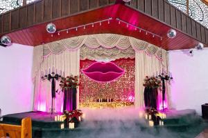 A wedding chapel with a stage featuring gold sequins, pink neon lips and green carpeting as smoke and fog effects start to flow throughout.