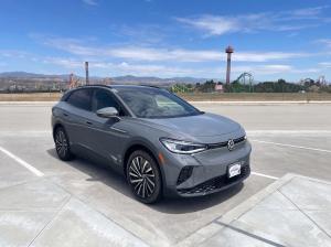 A gray Volkswagen ID.4 electric SUV parked in a lot at Valencia by FivePoint, with Six Flags Magic Mountain roller coasters and the surrounding mountains visible in the background.