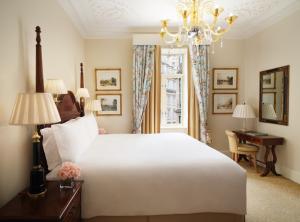 Luxury bedroom furniture inside a Savoy Hotel London suite as seen in Savoy Sale (3).jpg, featuring a pristine king-size bed, polished light-wood bedside tables with matching vanity desk, sculptural wall sconces, and an elegant window seating area.