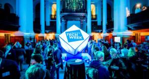 Attendees networking at a London Tech Week event, with the London Tech Week logo displayed in a large illuminated installation at the centre of the venue.