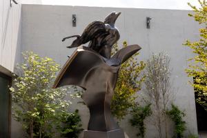 A bronze sculpture of a bird flying out of a book in a garden setting.